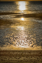 sunlight reflecting on wet sand on a beach 
