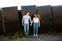 a couple holding hands in front of a metal wall 