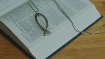 Close-Up of Opened Bible Book with Psalms Text and Ichthus Necklace