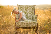 Happy girl sitting on big chair in open field