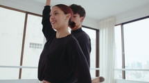 Young cheerful ballerina practicing pirouette with partner in dance studio: standing on demi-pointe and holding arabesque pose with arm up, boy turning her around. Tilt-up shot
