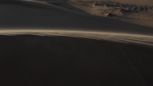 Sun glistening sand blowing in desert wind. Wind blowing sand and dust over middle eastern desert sand dunes in United Arab Emirates landscape during evening sunset in cinematic slow motion.