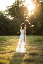 back of a woman in a white dress walking in the grass 