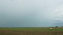 Distant lightning strike in storm clouds. Farmland landscape with hay bales and distant thunderstorm with lightning bolt flash.