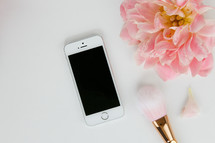 pink flower, iphone, and makeup brush on a white background 