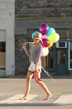 a teen girl walking carrying her shoes and balloons
