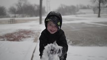 Happy young boy playing in cinematic slow motion in the snow while it's snowing outside on Christmas morning smiling at the camera.