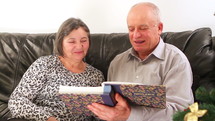 Elderly couple talking near a Christmas tree and looking at a photo album 