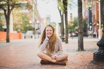 a young woman sitting on a brick sidewalk 