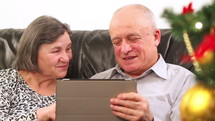 Elderly couple talking near a Christmas tree and using a tablet 
