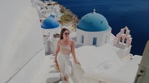 A beautiful tourist woman enjoying view at the blue domed church of the village of Oia, Santorini, Greece, during her summer holidays
