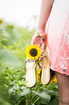 woman carrying sandals through a field of sunflowers 