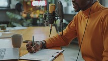 Male Blogger Recording Audio Podcast and Taking Notes on Paper
