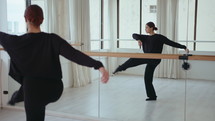 Young beautiful girl performing expressive contemporary dance during rehearsal in studio with mirror wall
