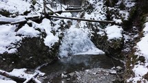 Wooden Bridge Over A Cold Mountain Stream In A Winter Forest  - wide shot