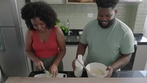 In Kitchen: Perfectly Happy Black Couple Preparing cake. Makes Her Girlfriend Laugh. Lovely People in Love Have Fun
