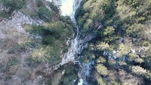 Top View Of Frozen River Flowing Between Forest Mountains In Winter. Aerial Drone Descending