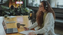 Young Female Journalist Using Laptop and Planner during Podcast Recording
