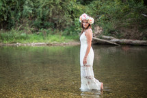 a woman in a white dress and flowers in her hair walking in water 