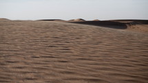 Sun glistening sand blowing in desert wind. Wind blowing sand and dust over middle eastern desert sand dunes in United Arab Emirates landscape during evening sunset in cinematic slow motion.