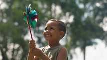 kid with colorful pinwheel. little baby boy play with windmill toy wind in the park. happy family kid dream concept. Toddler play toy pinwheel in a sunny day at the park