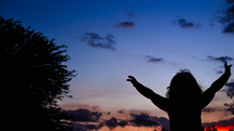 silhouette of a child with raised hands at sunset 