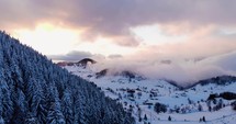 Aerial Drone Shot of Coniferous Forest On Mountainous Landscape Densely Covered With Fresh Snow During Winter At Sunset. 