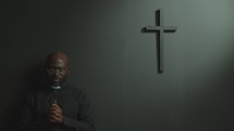 Black Priest Praying to God with Eyes Closed in Modern Minimalist Church