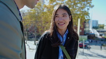 Company of young cheerful coworkers standing together outdoors on sunny day, smiling and chatting, gathering together after work
