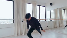 Young Hispanic male dancer practicing classical ballet movements with graceful arms and good posture in modern studio with barre and glass wall
