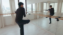 Young creative male dancer improvising and performing contemporary dance in front of mirror wall in a dance studio
