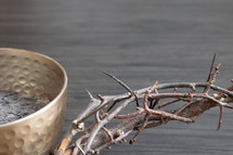 Partial crown of thorns and bowl of ashes on a dark wood background with copy space