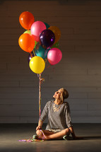 a woman holding balloons sitting on the floor 