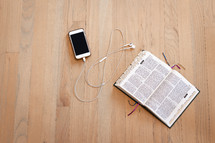 open Bible and phone with earbuds on a wood floor 