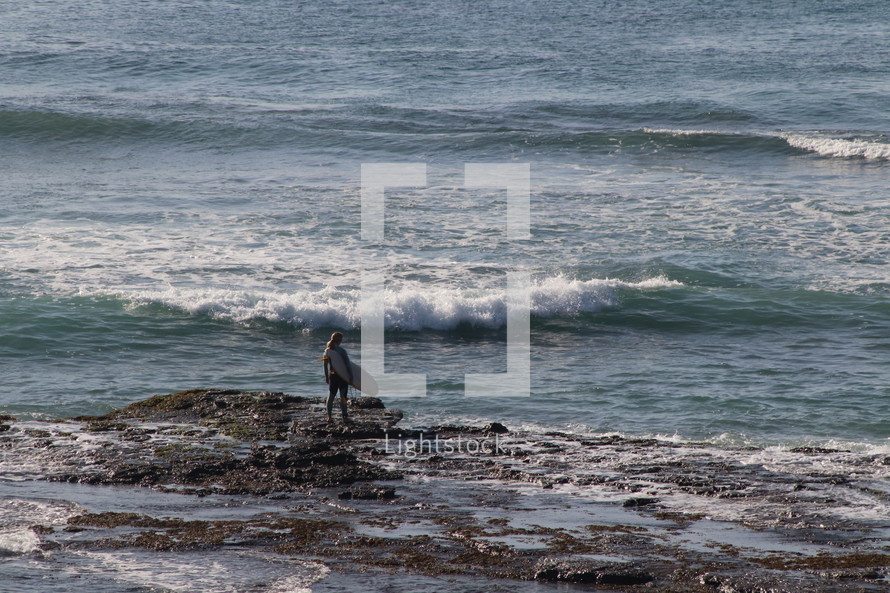surfer standing on a rocky shore 