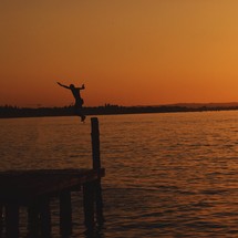 a boy jumping off a dock at sunset 
