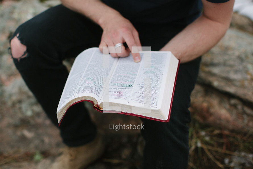 a man sitting on a rock on a mountaintop reading a Bible 
