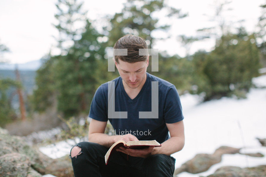 a man reading a Bible sitting on a rock on a mountaintop 