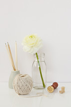 white flower in a clear vase, yarn, stamp, wooden spool 