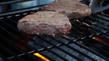 Steaks Being Turned on a Barbecue Grill with Lid Closing