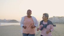 Morning activity for seniors. Positive mature women friends wearing sport clothes running together outdoors, training early on sport ground, slow motion
