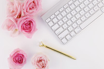 pink roses, gold pen, and keyboard on a white desk 