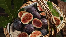 Fresh ripe figs harvest in wicker basket with leaves, rustic wooden table serving. Ficus carica. Beautiful sweet seasonal fruits, vegan food. Top view. Dolly slider shot. High quality 4k footage