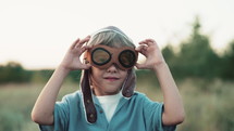 Portrait of funny little boy in aviator helmet wearing protective eyeglasses and ready to fly as airplane. Kids dream is to be pilot. 