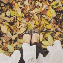 Feet in leopard fabric shoes standing in fall leaves.
