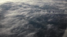 View of earth and clouds from airplane window while flying in cinematic slow motion above the clouds in the atmosphere.