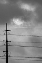 power lines, sun and clouds in the sky in black and white