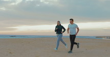 Young man and woman having running on the beach wearing headphones.