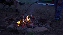 A man stoking up a campfire with a stick