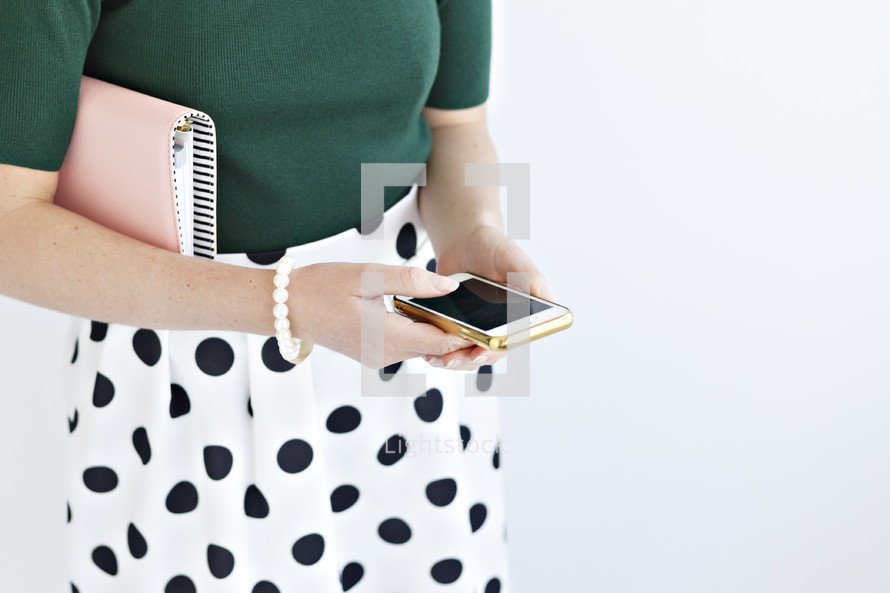 a woman holding a planner and looking at a cellphone 